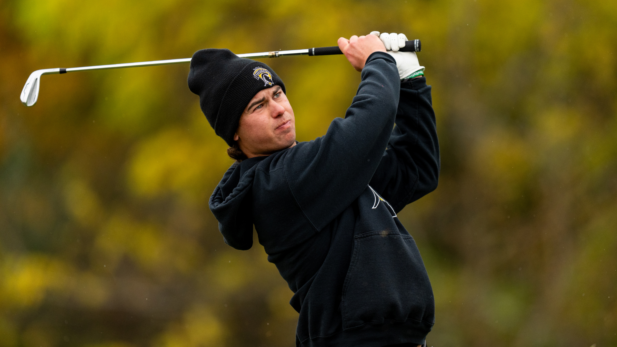 Man in navy blue swinging a golf club with an out of focus green background