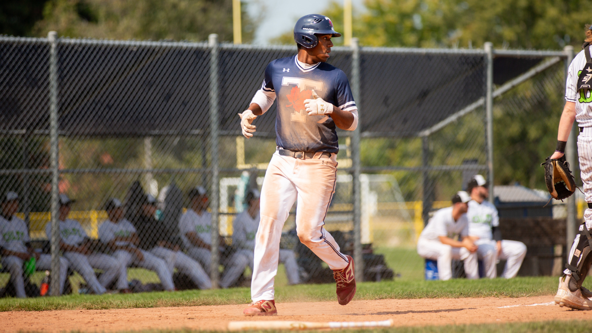 young man in focus running on a baseball field with dirt on his uniform