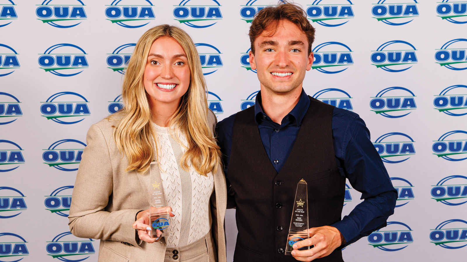 OUA athletes of the year Sara Rohr and Max Davies posing with their respective trophies in front of an OUA logo step-and-repeat backdrop