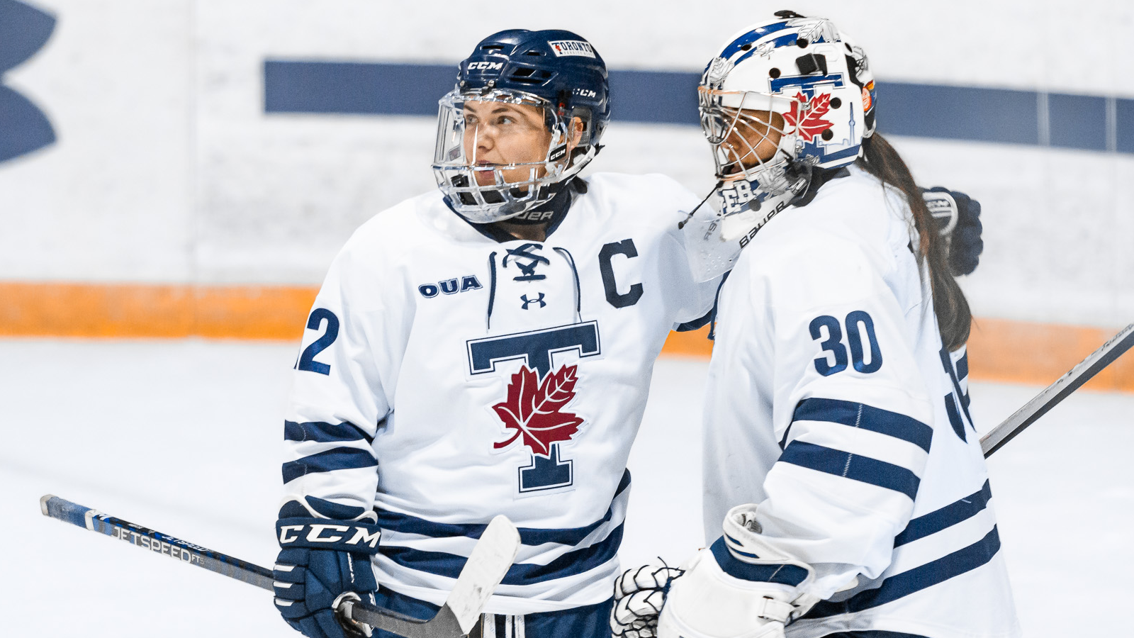 Two members of the Toronto Varsity Blues women's hockey team - one player and one goalie - with their arm around the other on the ice in celebration
