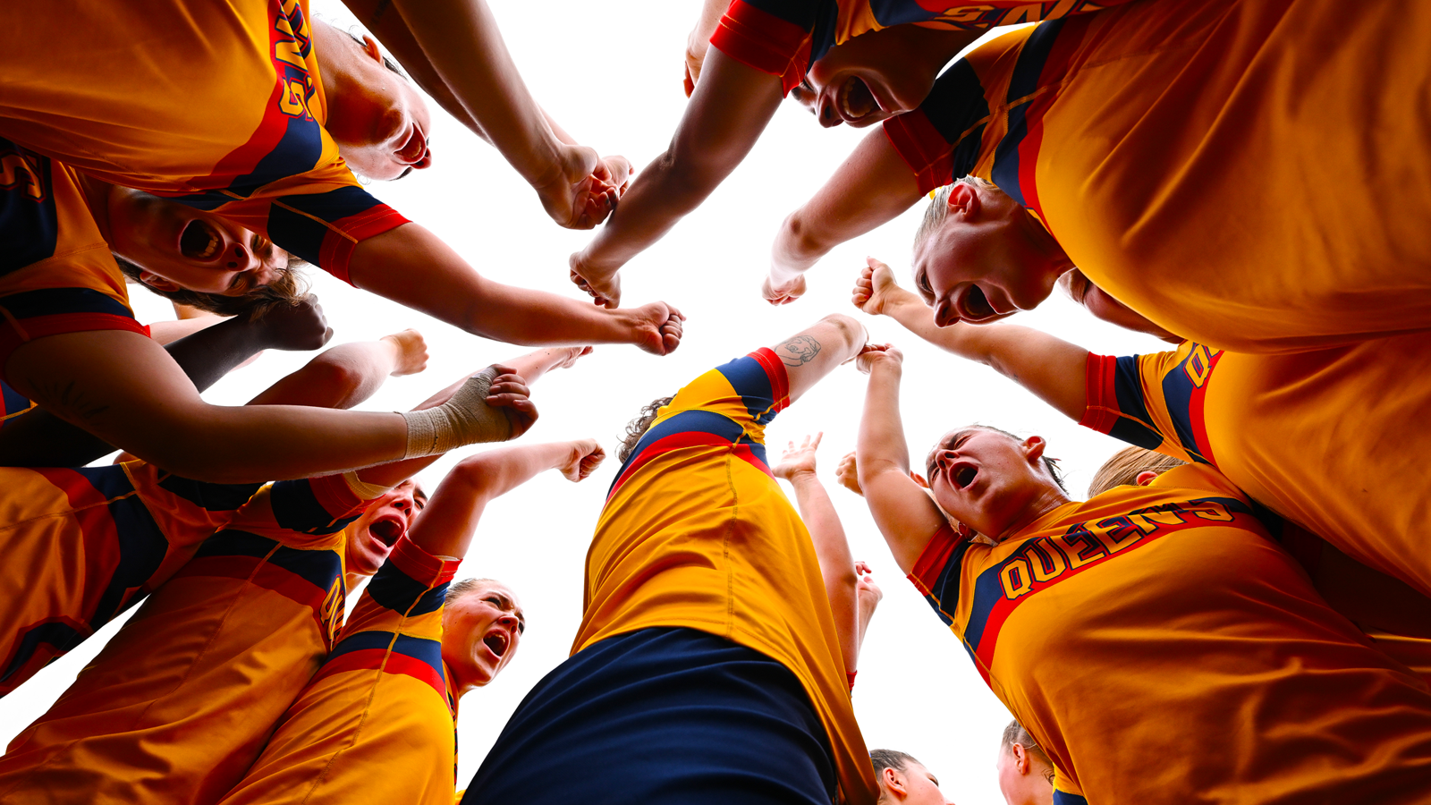 Queen's women's rugby team huddled together, each holding an arm up in the air for a cheer