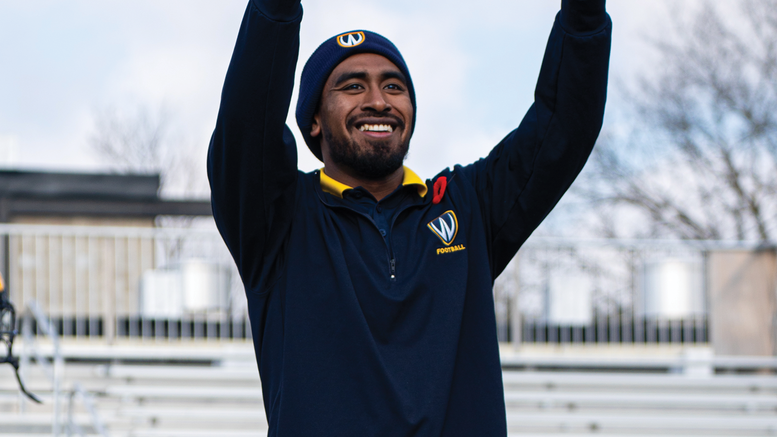 Windsor football coach Isaiah Johns standing on the field in school branded attire raising his arms