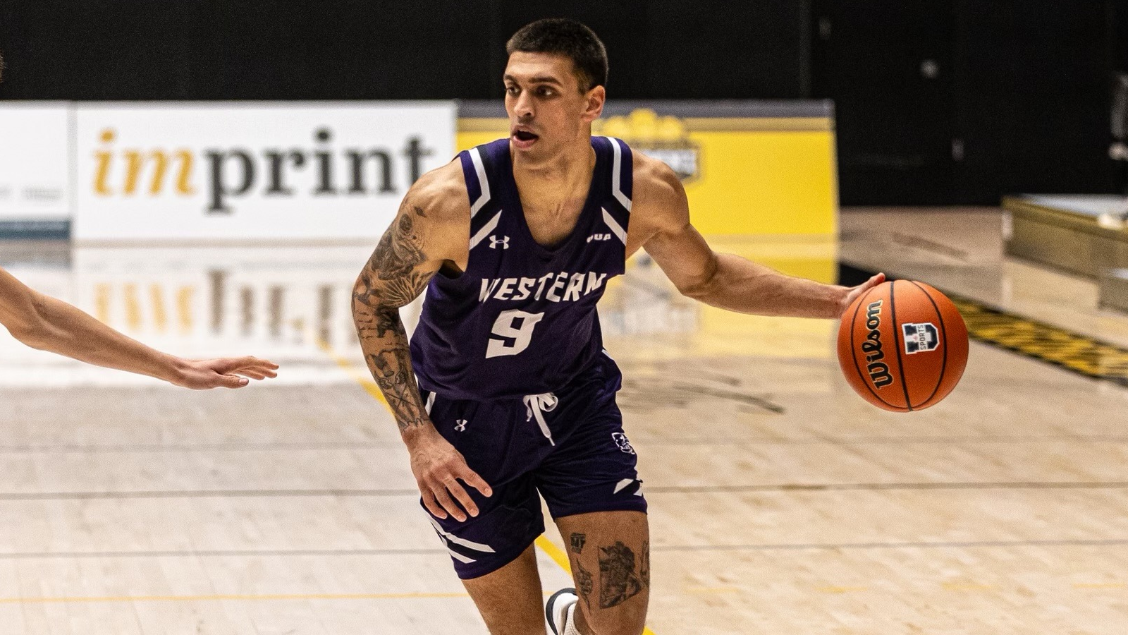 Western men's basketball player dribbling the ball off to his left side