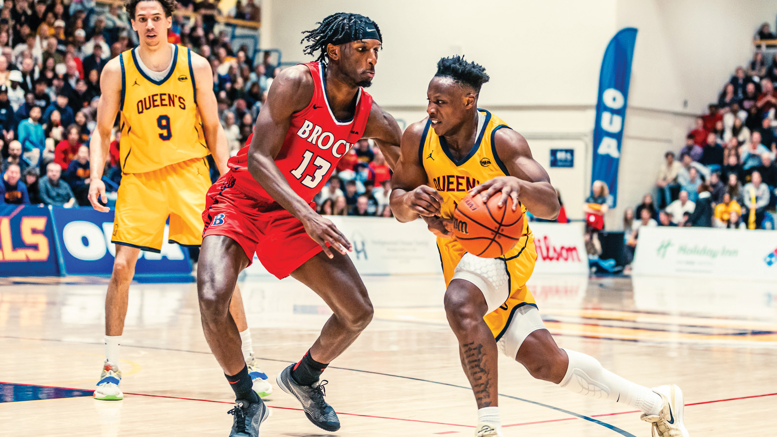 Queen's men's basketball player dribbling the ball into a Brock defender during the OUA championship game