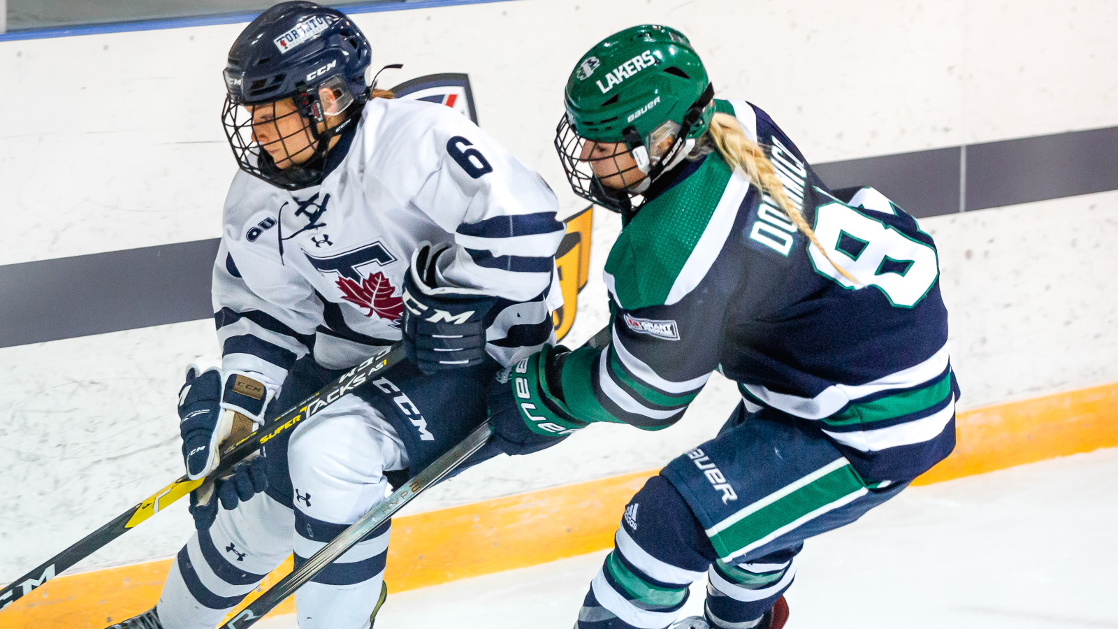 Toronto women's hockey player and Nipissing women's hockey player competing for the puck along the boards during a game